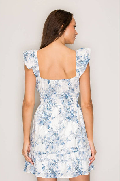 Woman wearing a white dress with blue floral pattern against a plain background