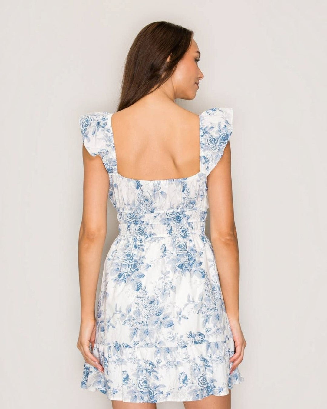 Woman wearing a white dress with blue floral pattern against a plain background