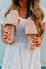 Person holding two pairs of beige sandals with decorative elements against a blurred background