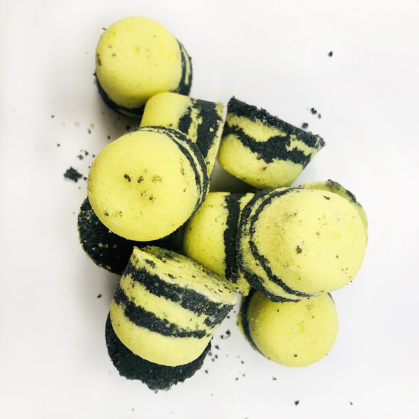 A handful of our yellow and black striped bumblebee buzz bath bombs piled up on eachother against a white background