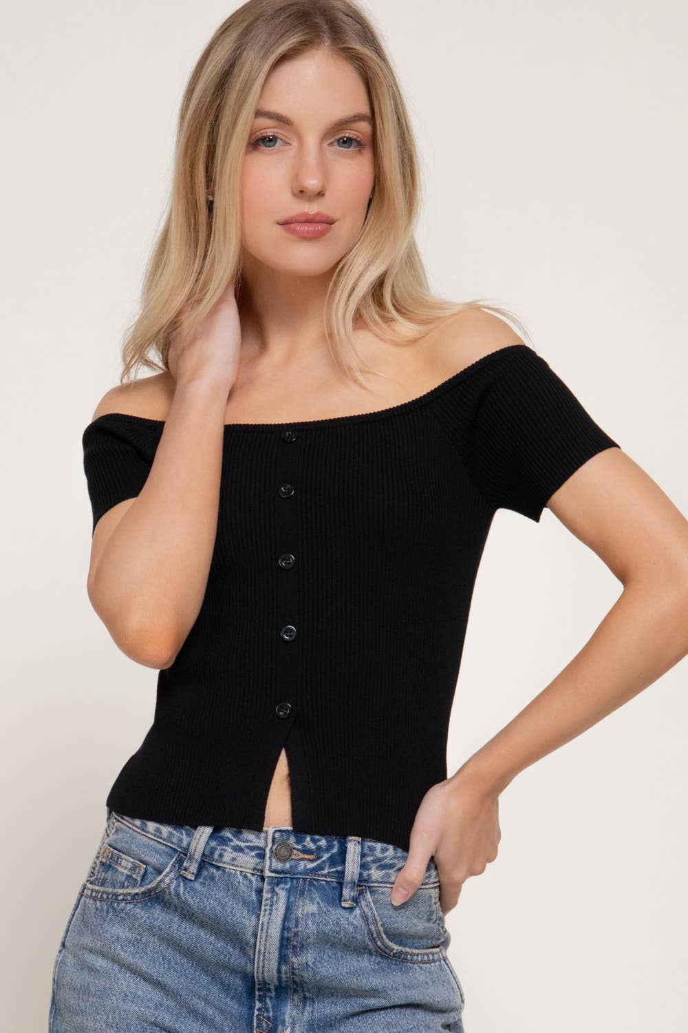 Woman wearing a black off-shoulder top and blue jeans against a white background