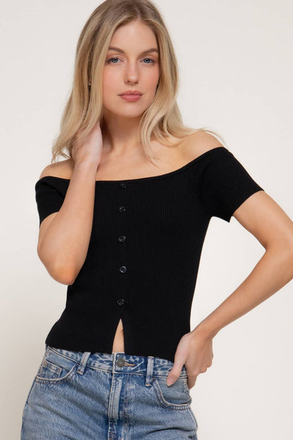 Woman wearing a black off-shoulder top and blue jeans against a white background
