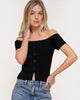 Woman wearing a black off-shoulder top and blue jeans against a white background