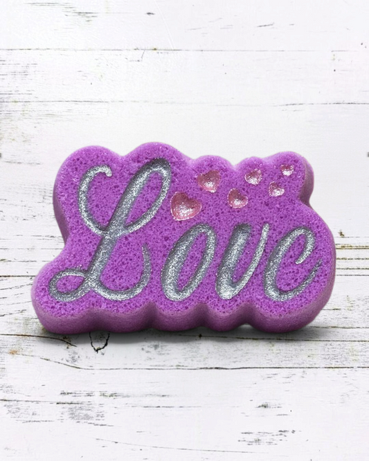 Calla Lily Cosmetics + CL kids purple Love bath bomb with silver glitter lettering and heart accents on a marble shelf