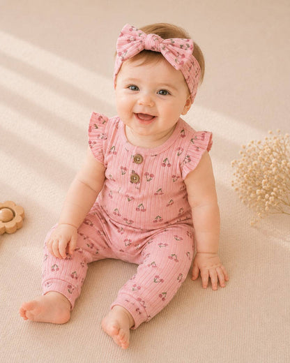 Baby in pink outfit with ruffled sleeves and matching headband, sitting on a beige surface.