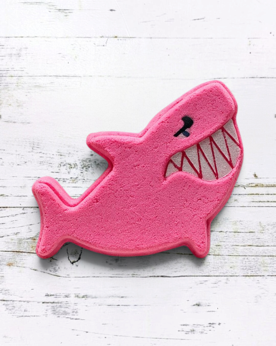 Calla Lily Cosmetics + CL kids pink shark-shaped bath bomb with strawberry scent on a white wooden background.