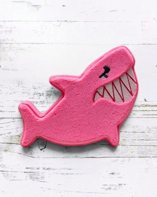 Calla Lily Cosmetics + CL kids pink shark-shaped bath bomb with strawberry scent on a white wooden background.
