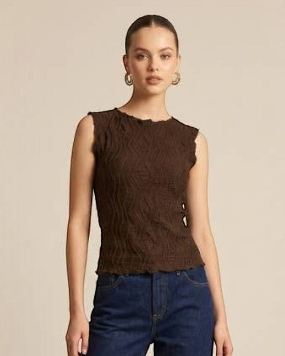 Woman wearing a brown sleeveless top and blue jeans on a beige background
