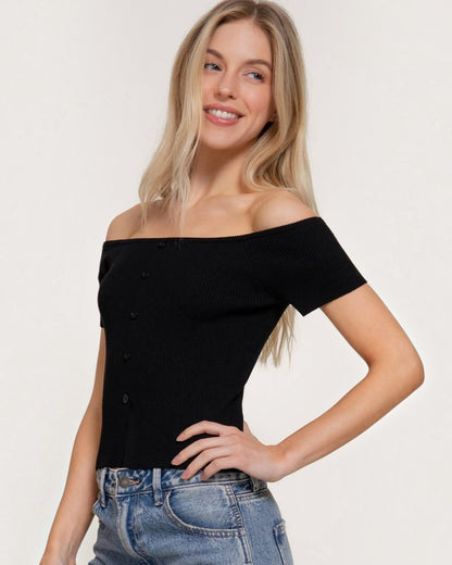 Woman wearing a black off-shoulder top and blue jeans on a plain background