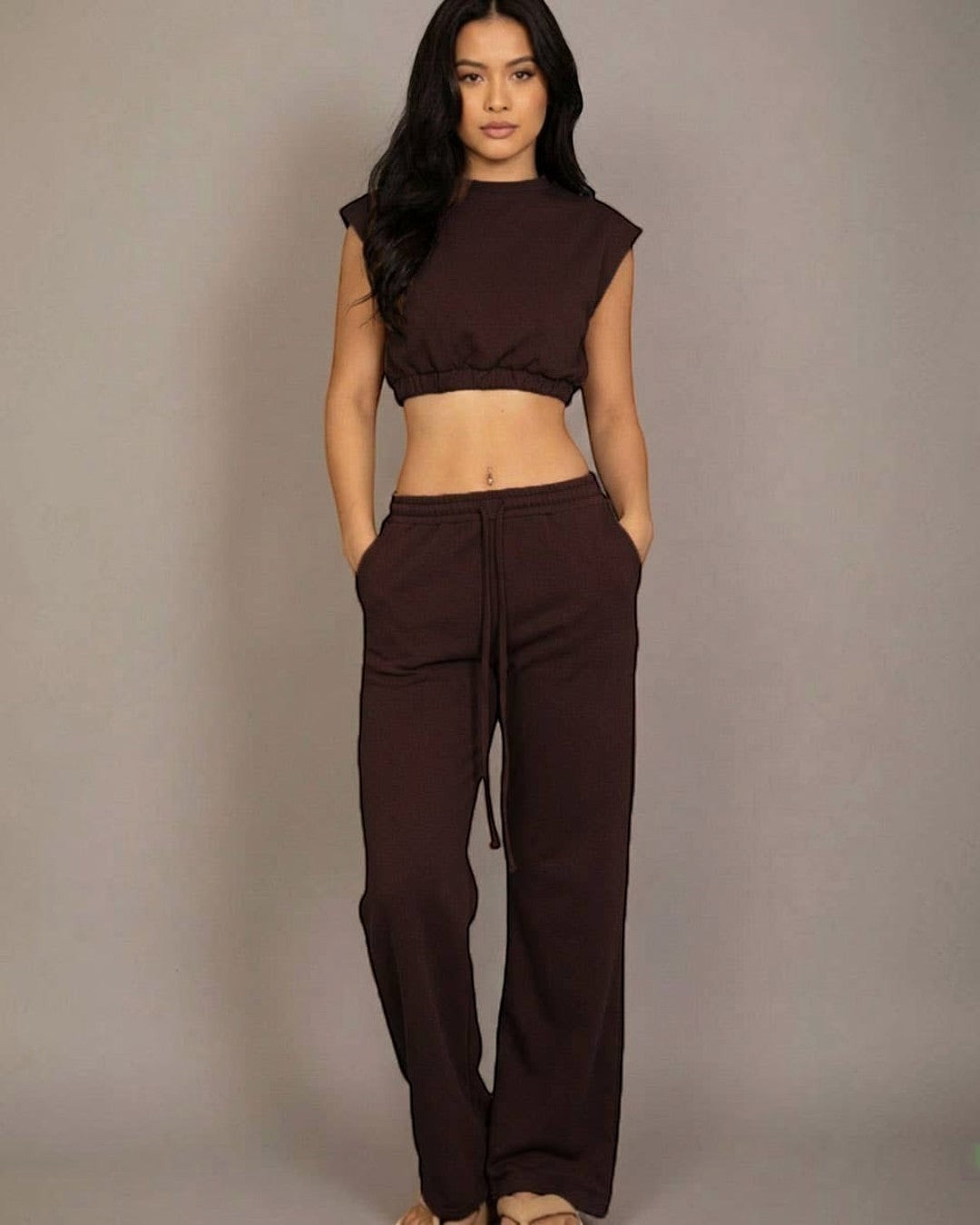 Woman wearing a brown sleeveless top and pants against a gray background