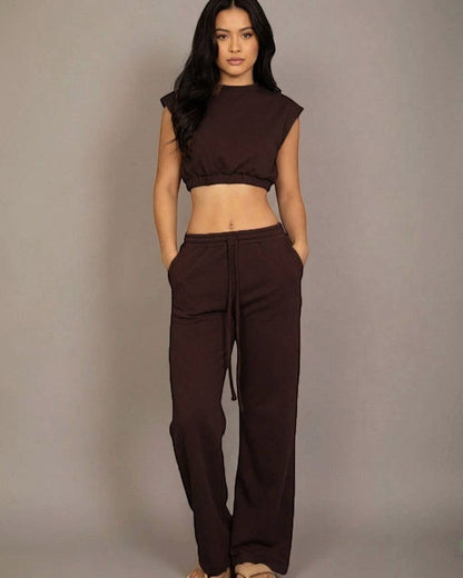 Woman wearing a brown sleeveless top and pants against a gray background