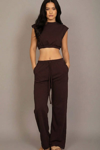 Woman wearing a brown sleeveless top and pants against a gray background