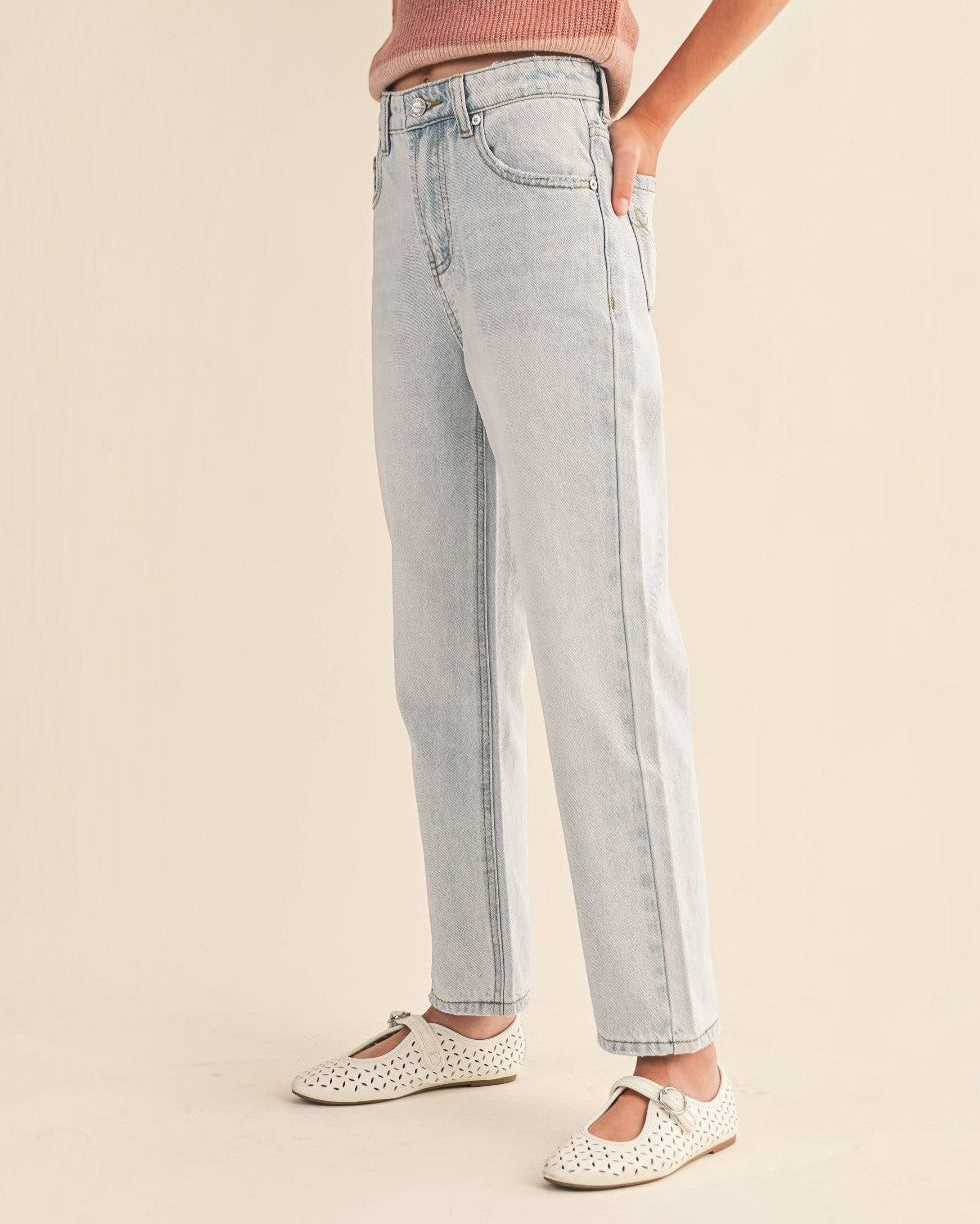 A person wearing light-wash straight-leg denim jeans, a pink ribbed top, and white Mary Jane flats, standing against a plain beige studio background.