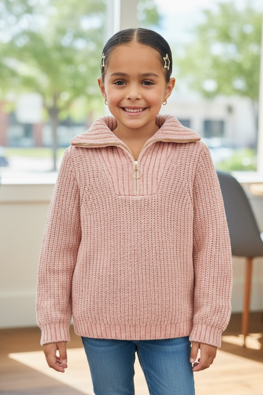 Young girl wearing a pink knit sweater and blue jeans indoors.