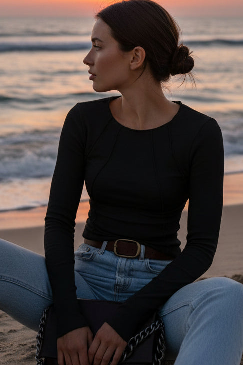 Person wearing a black long-sleeve top and blue jeans, holding a brown handbag with a chain detail.