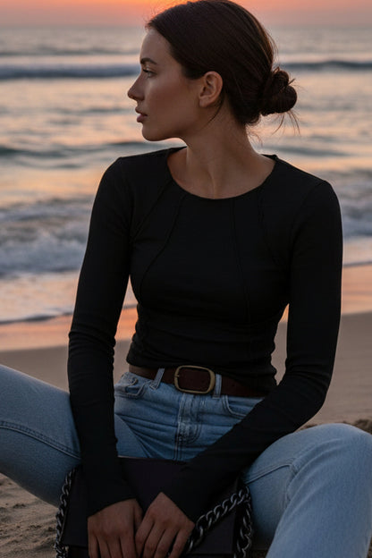 Person wearing a black long-sleeve top and blue jeans, holding a brown handbag with a chain detail.