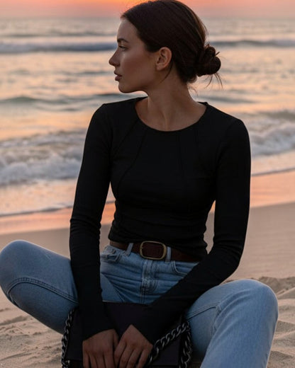 Person wearing a black long-sleeve top and blue jeans, holding a brown handbag with a chain detail.