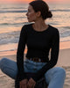 Person wearing a black long-sleeve top and blue jeans, holding a brown handbag with a chain detail.