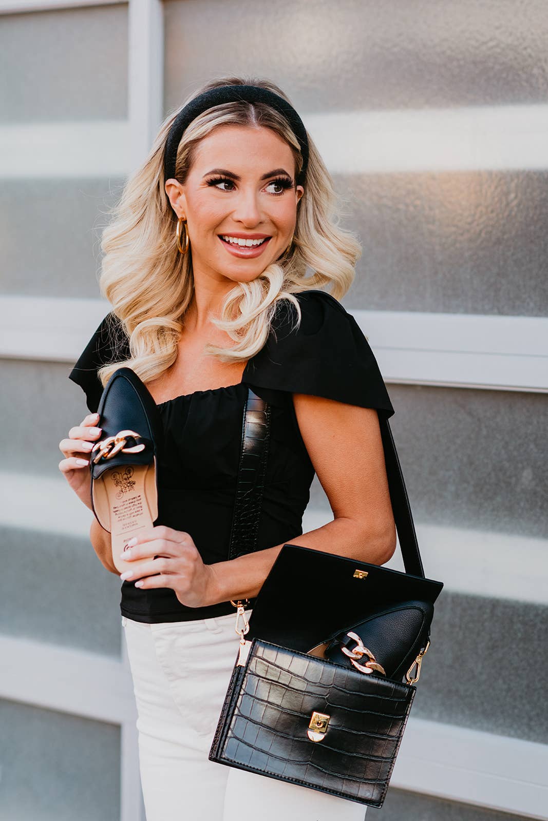 Woman holding a black handbag with gold accents against a neutral background