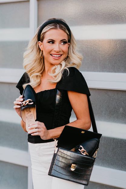 Woman holding a black handbag with gold accents against a neutral background