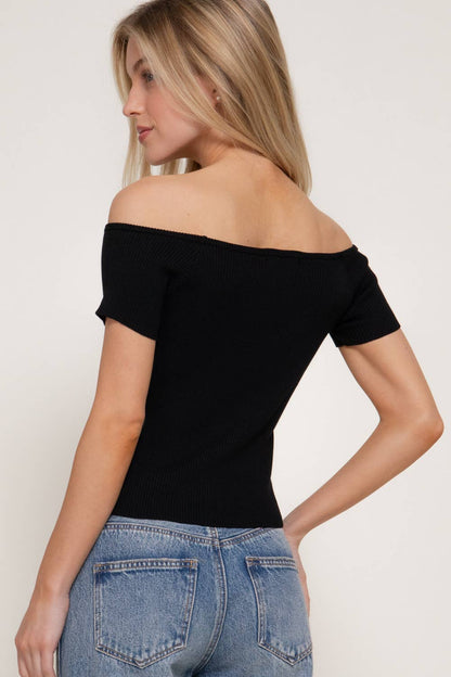 Woman wearing a black off-shoulder top and blue jeans on a white background