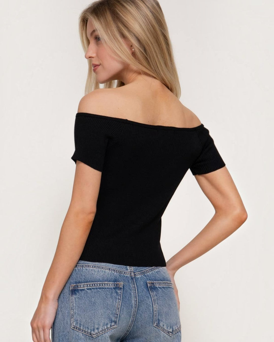 Woman wearing a black off-shoulder top and blue jeans on a white background