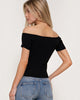 Woman wearing a black off-shoulder top and blue jeans on a white background