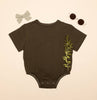 Brown baby onesie with leaf design, gray bow, and sunglasses on beige background