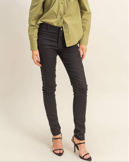 A woman modeling a long-sleeve olive green blouse with a unique gathered front and black skinny jeans, paired with black strappy high heels, against a plain beige studio background.
