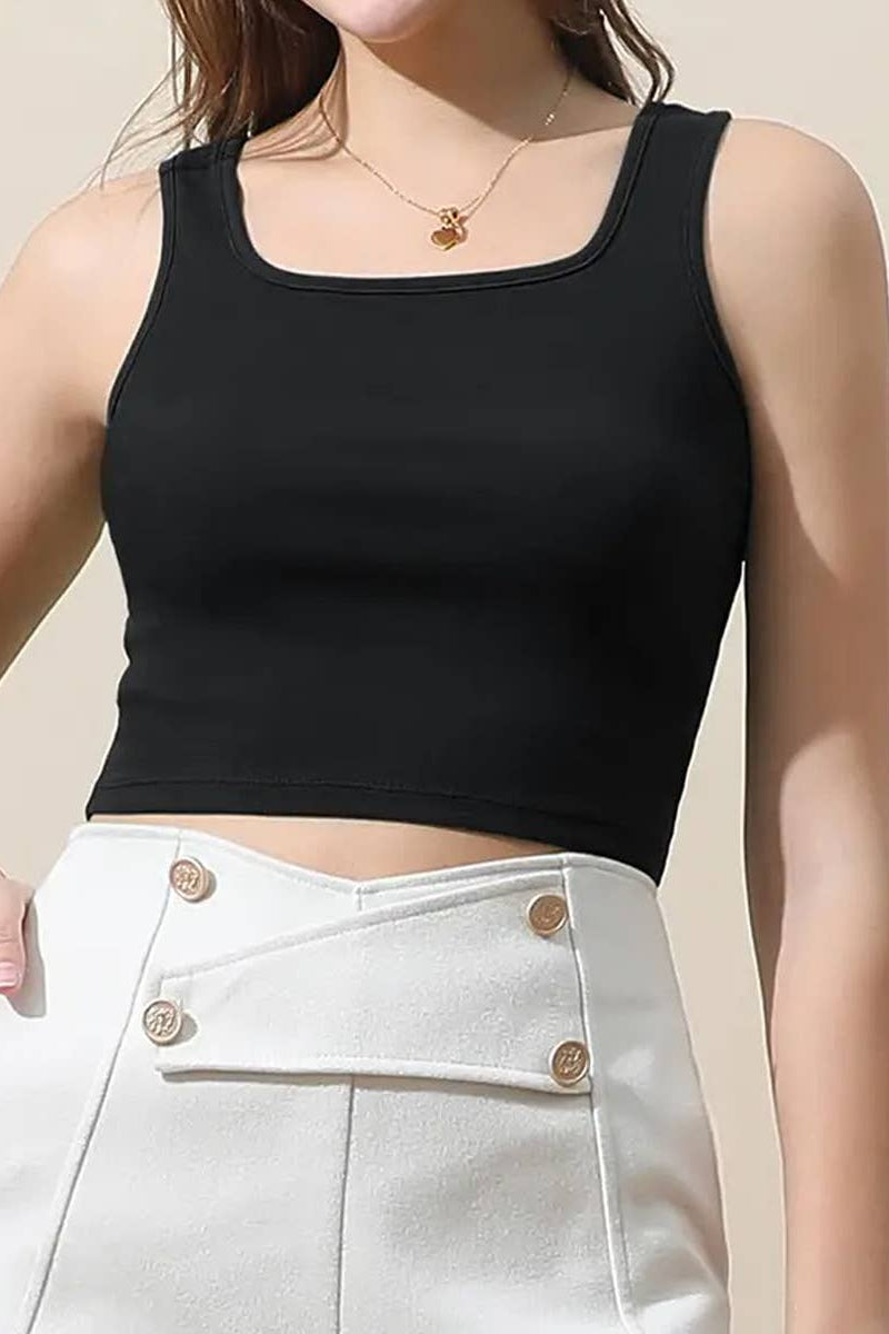 Person wearing a black tank top and white pants with gold buttons on a beige background