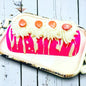 A pink twinkie bath bomb topped with white frosting and sugar sprinkles on a white tray