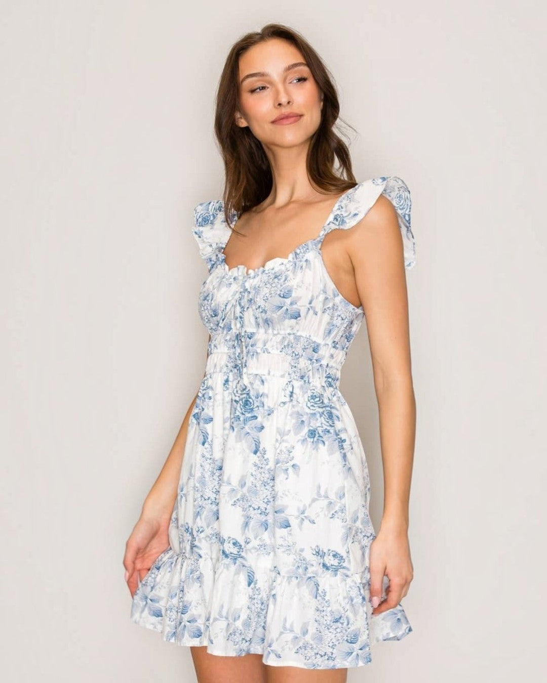 Woman wearing a white dress with blue floral patterns against a plain background