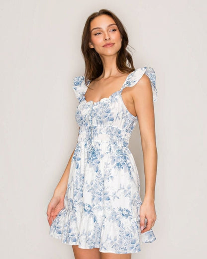Woman wearing a white dress with blue floral patterns against a plain background