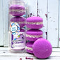 A stack and tube of 4 purple unicorn yawns bath cookies against a wood background