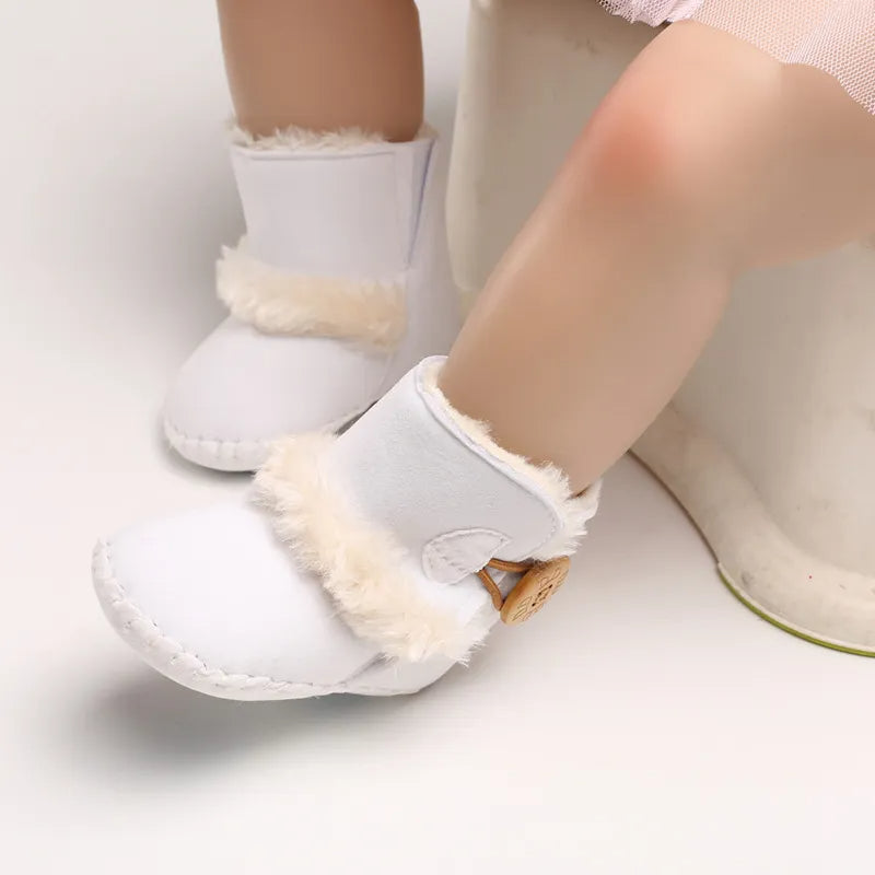 White baby shoes with fur trim worn by a child on a light background