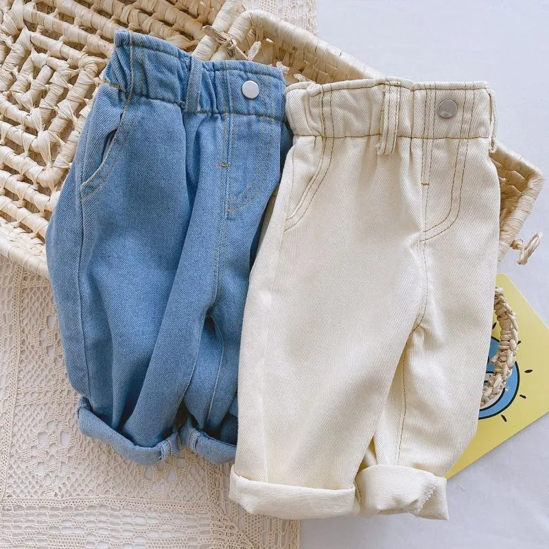 Two pairs of children's pants, one blue and one beige, on a textured surface.