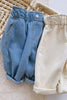 Two pairs of children's pants, one blue and one beige, on a textured surface.