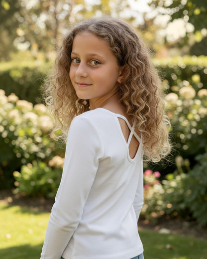 Young girl with curly hair wearing a white long-sleeve top in a garden setting