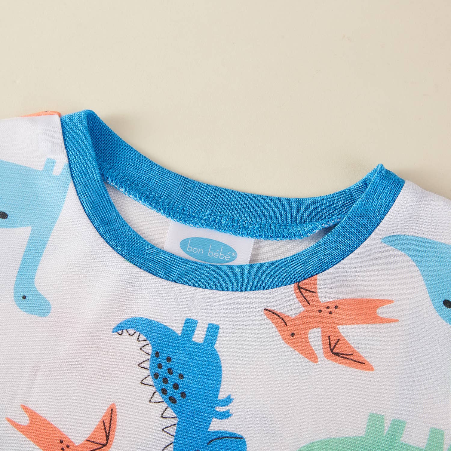 Children's pajama top with dinosaur pattern and blue collar on a beige background