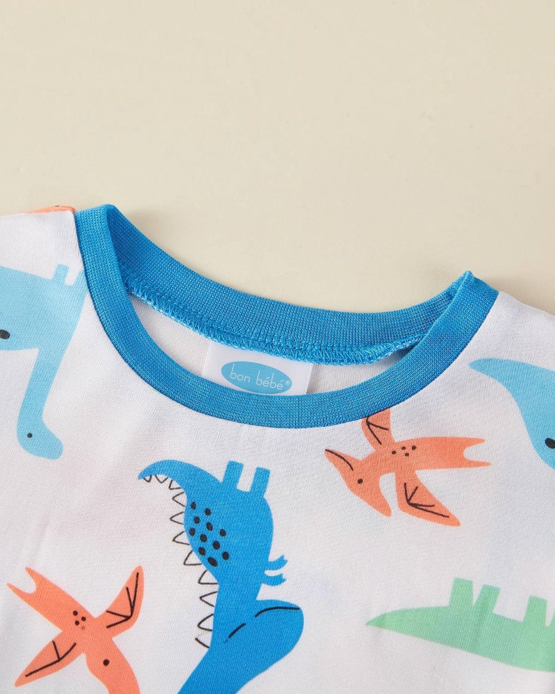 Children's pajama top with dinosaur pattern and blue collar on a beige background