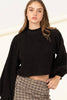 Woman wearing a black sweater and plaid pants on a plain background