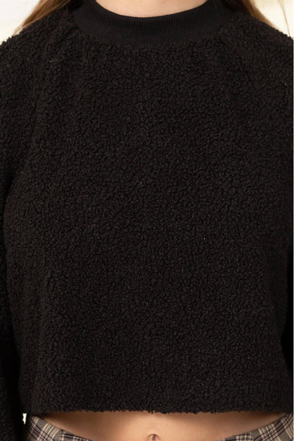 Black textured sweater worn by a person on a white background