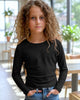 Young girl wearing a black long-sleeve shirt and blue jeans indoors.