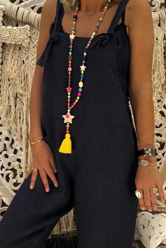 Person wearing a navy jumpsuit with colorful jewelry against an ornate stone wall.