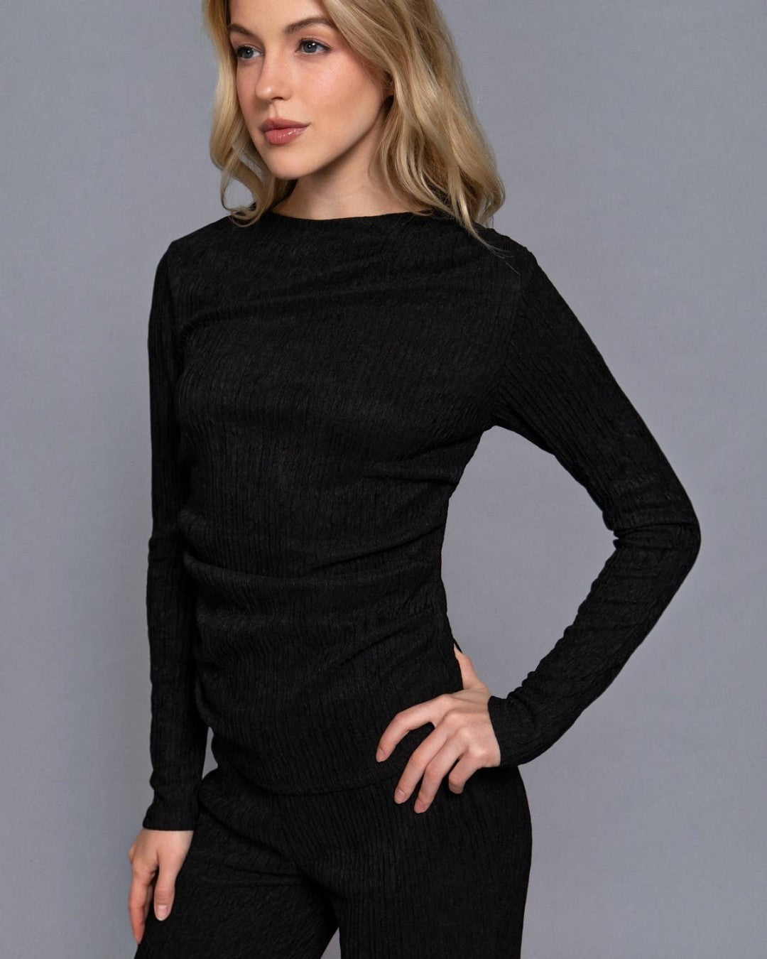 Woman wearing a black long-sleeve top against a gray background