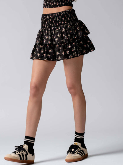 Person wearing a black floral skirt with ruffles on a gray background