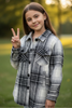 Young girl in a plaid shirt making a peace sign outdoors