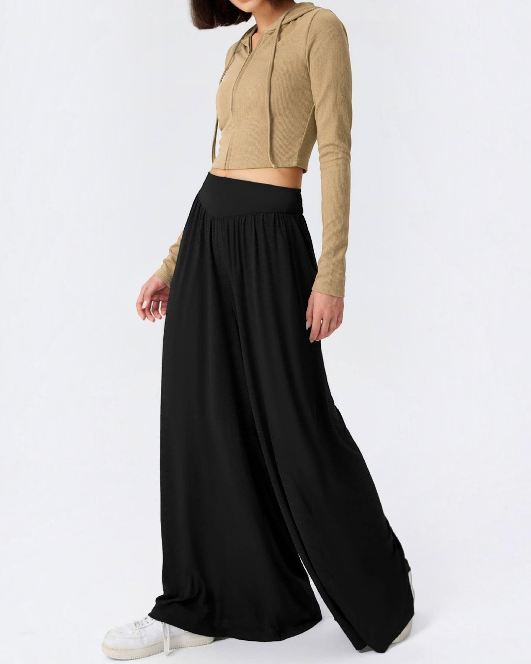 Person wearing a beige cropped hoodie and black wide-leg pants on a white background