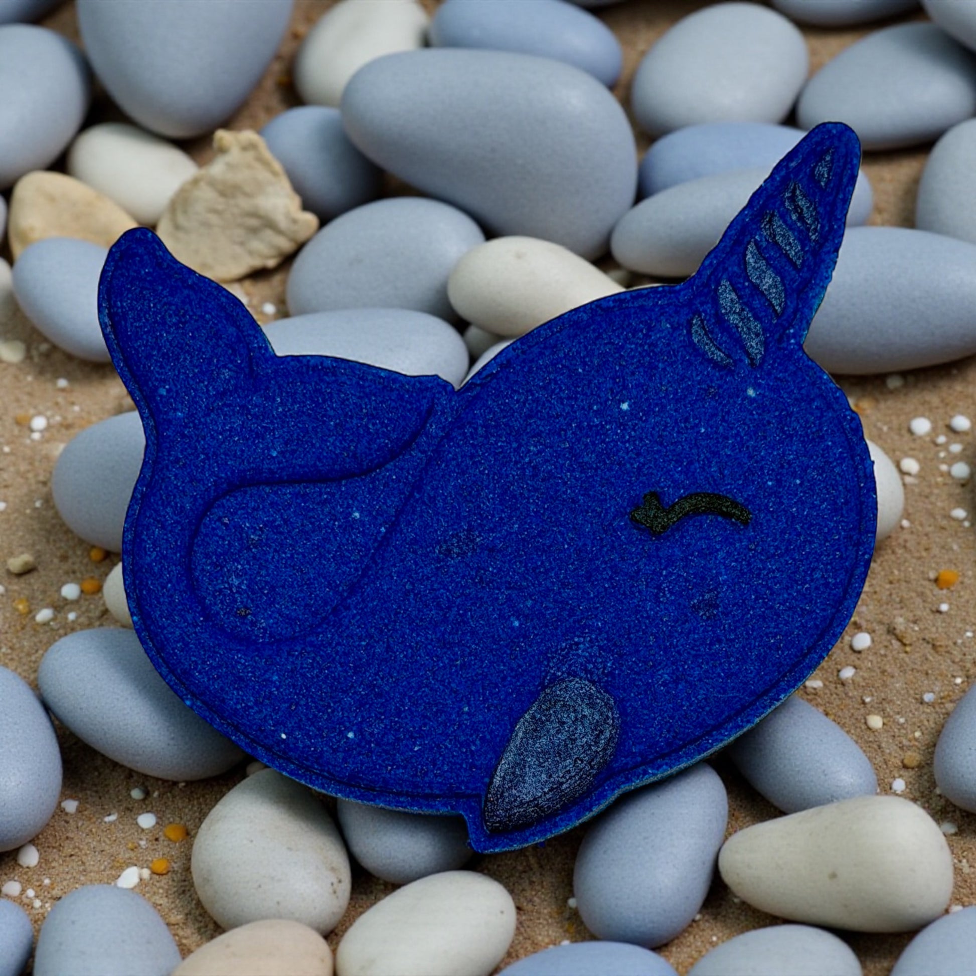 Blue felt narwhal toy on pebbles