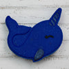 Blue felt narwhal toy on pebbles